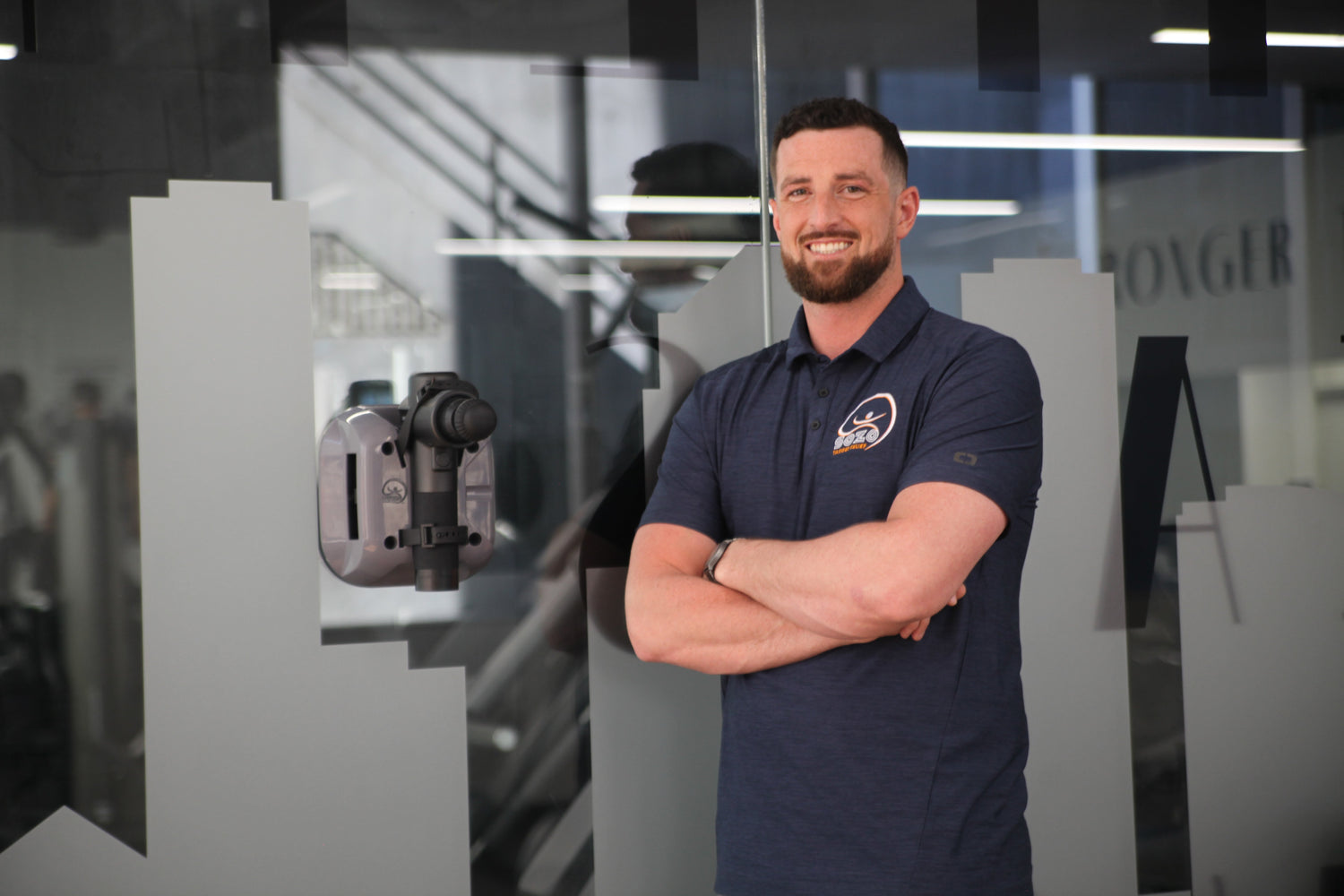 Man in a dark blue polo shirt standing in a modern office setting.